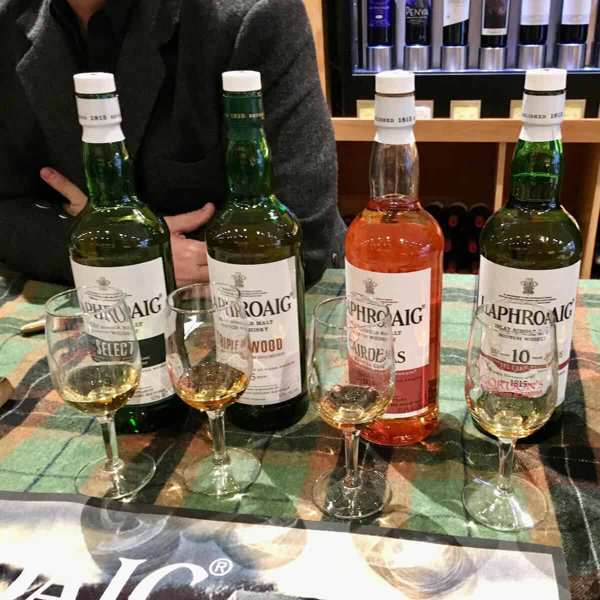 Lineup of Laphroaig scotch whisky poured into glasses with bottles behind on a green checked cloth.