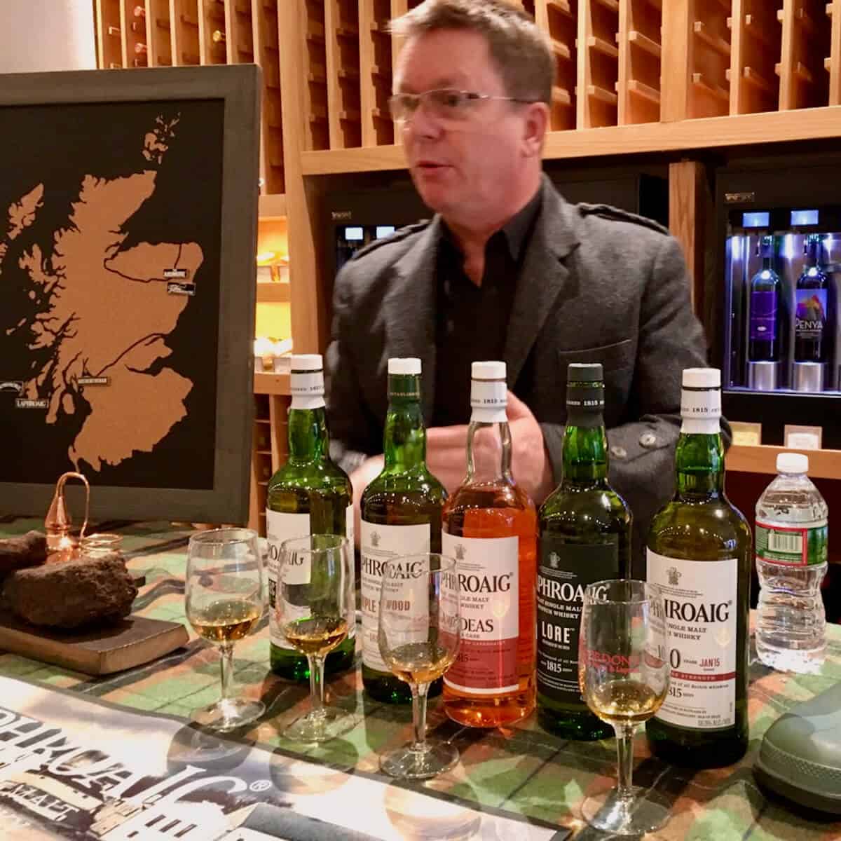 Simon Brooking behind the Laphroaig tasting lineup of glasses & bottles on a green checked cloth.