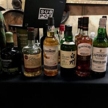 Peated whisky lineup bottles on a table next to a boot & tartan.