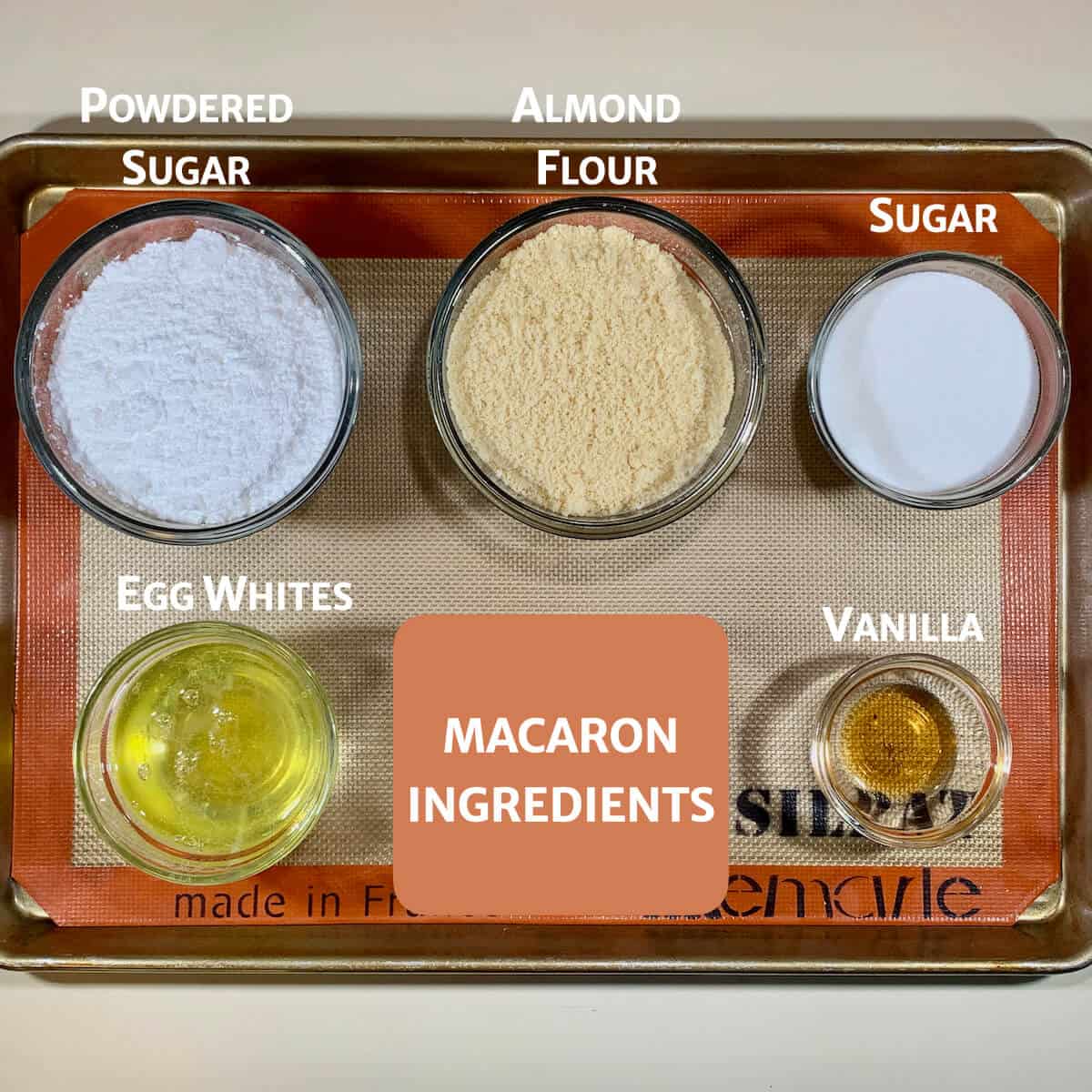 Macarons ingredients portioned int o glass bowls on a baking pan.