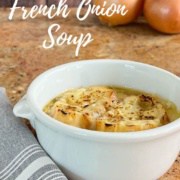 French Onion Soup in a bowl next to a spoon on a grey napkin with onions behind Pinterest banner.