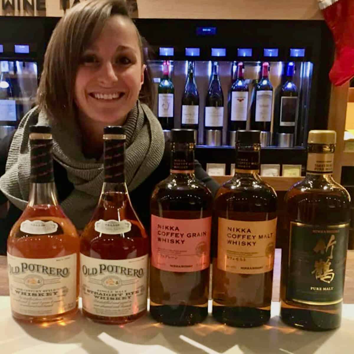 Kelly McCarthy behind Nikka Japanese whisky & Old Potrero Rye whiskey bottles on a counter.