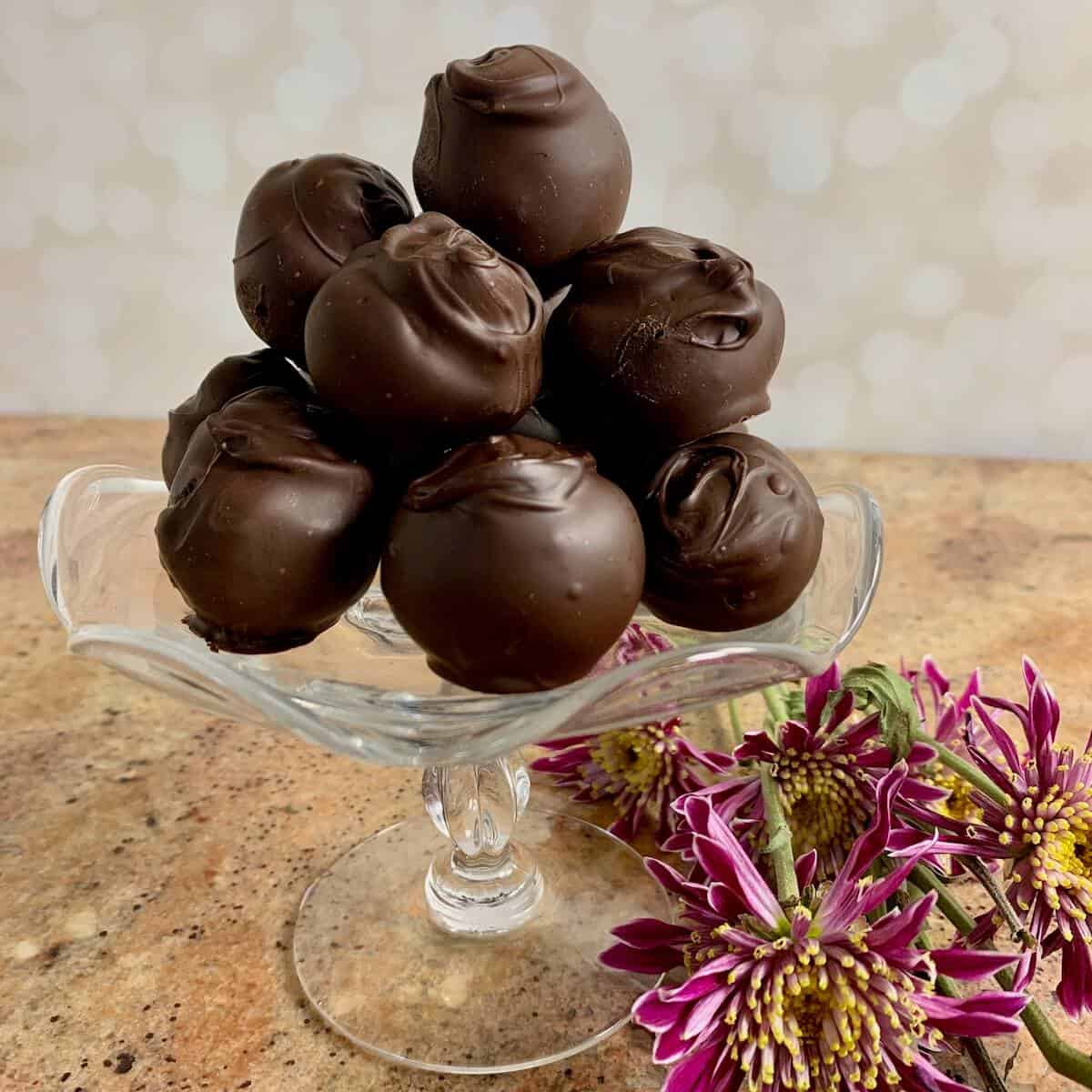 Chocolate cake truffles stacked on a glass plate stand with pink flowers below.