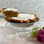 Butterscotch Pie with a sliced lifted on a glass cake stand and flowers below.