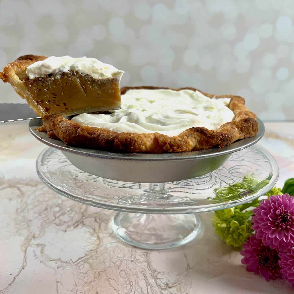 Whole Butterscotch Pie with lifted slice and flowers behind Pinterest banner.