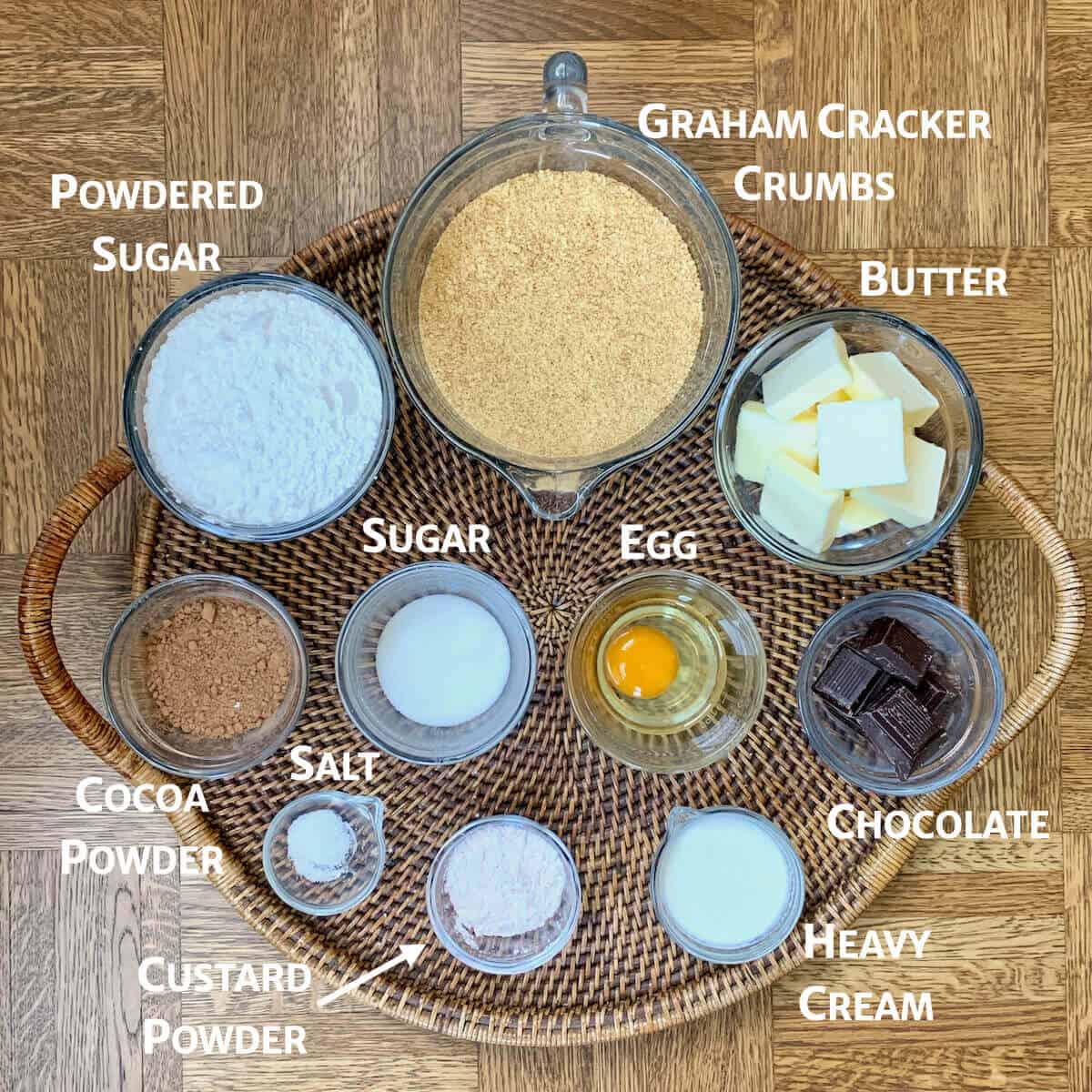 Nanaimo bars ingredients in portioned into glass bowls on a wooden tray.