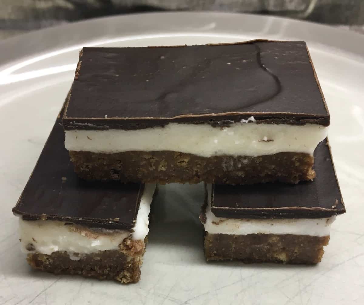 Nanaimo bars made without custard powder stacked on a white plate.