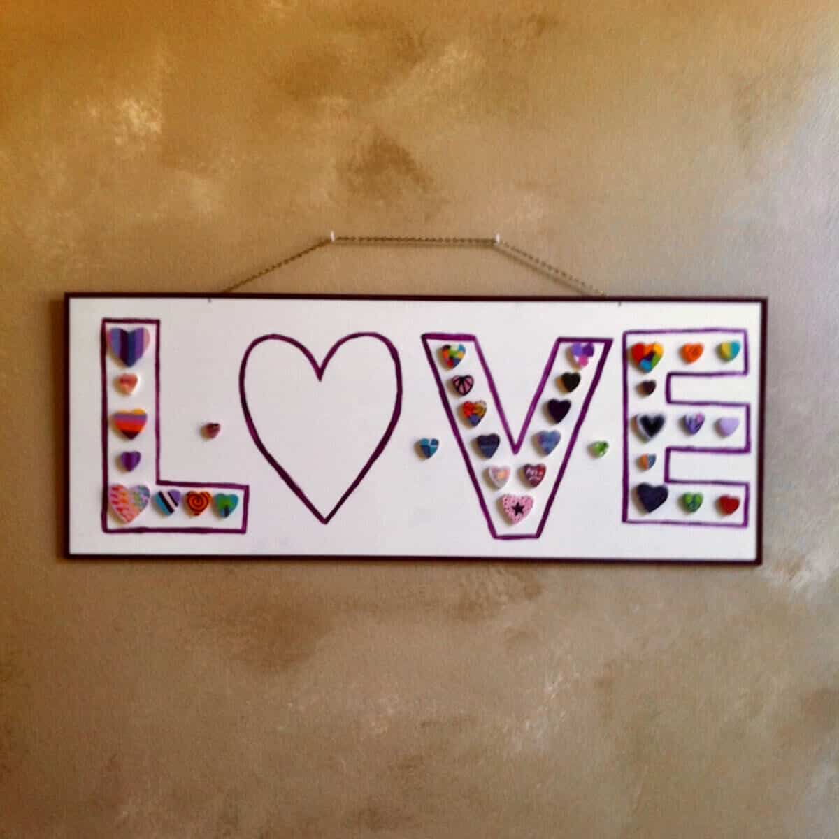 A handpainted sign saying Love hanging on a wall.