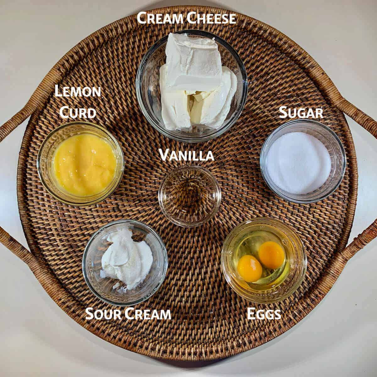 Lemon Curd Marbled Cheesecake filling ingredients portioned into glass bowls on a woven tray.