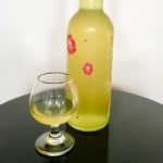 Homemade limoncello in a bottle and glass on a black table.