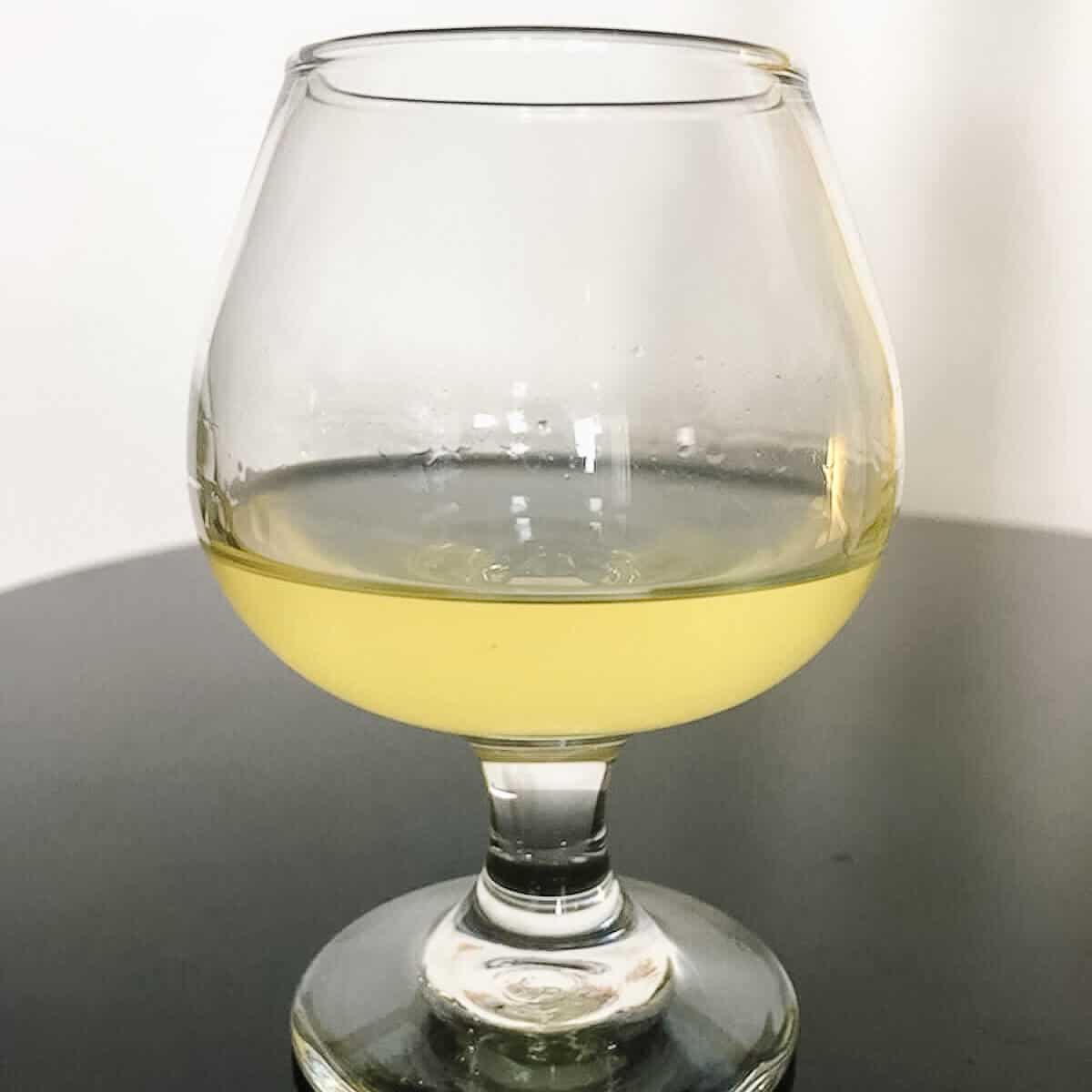 Homemade limoncello in a glass on a black table.