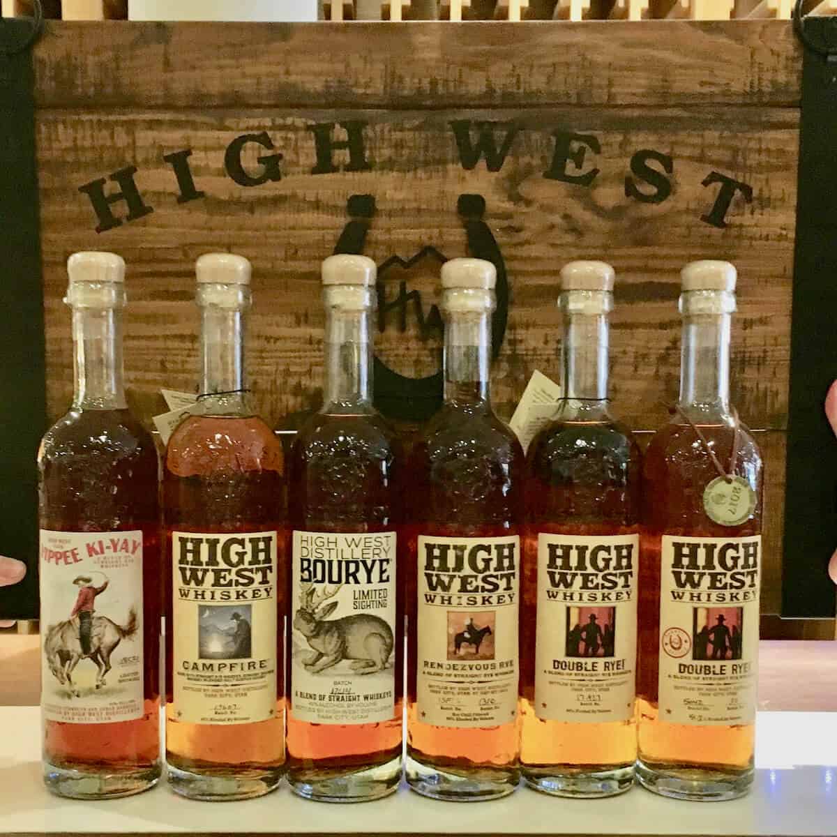High West Rye whiskey bottle lineup in front of wooden sign on a counter.
