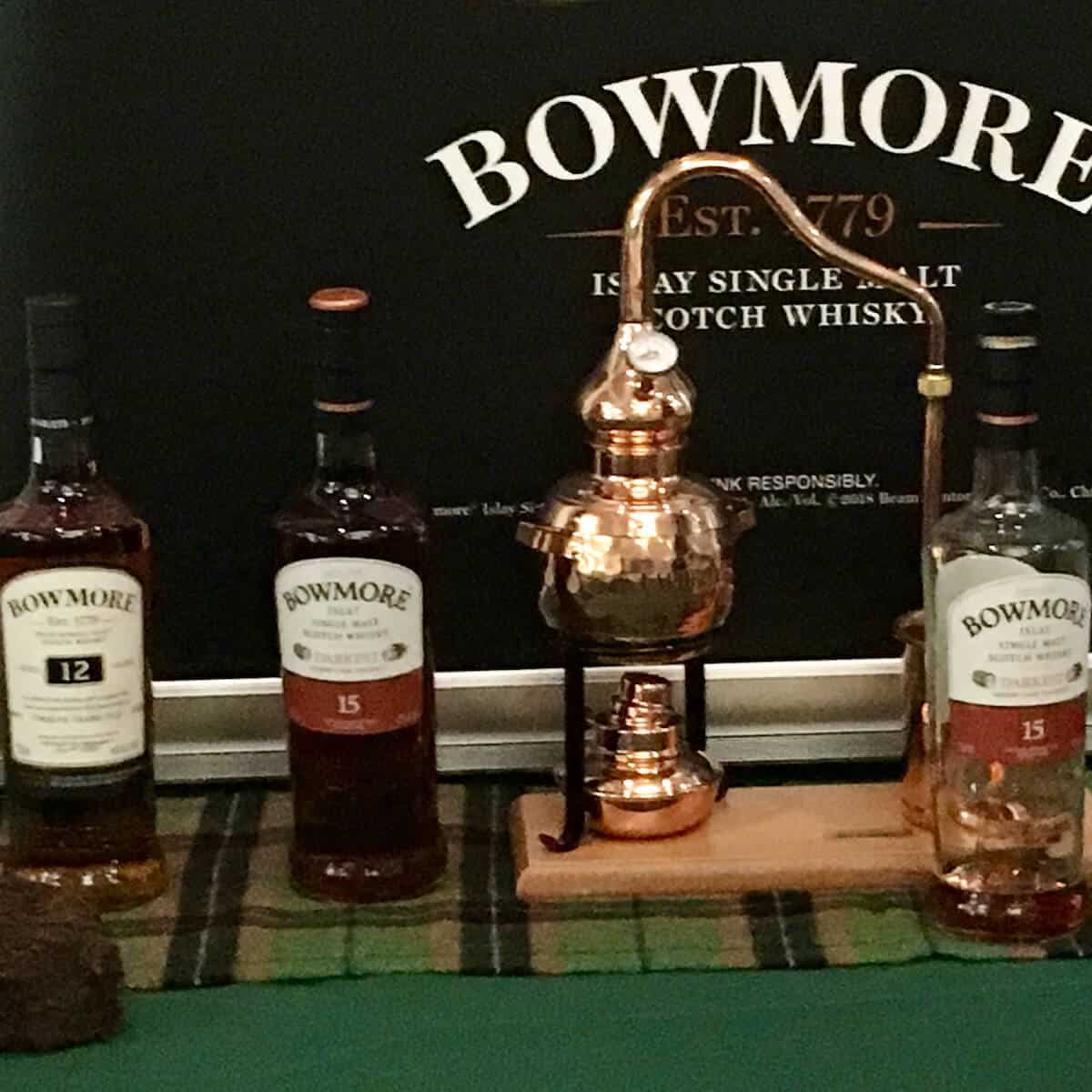 Bowmore lineup in bottles with model of a pot still.