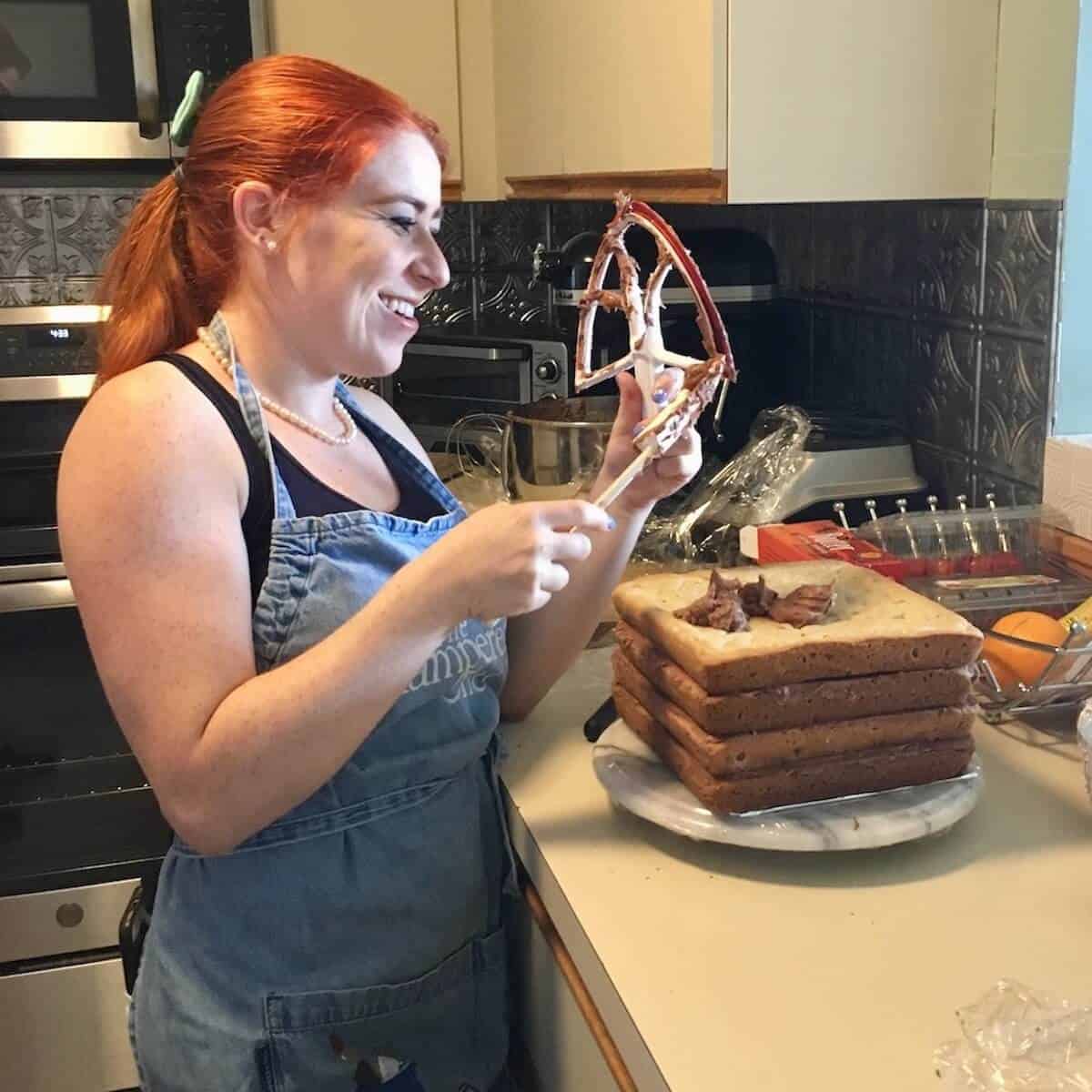 Author's younger daughter shown wiping mixer blade for frosting and stacking the cookie cake layers.