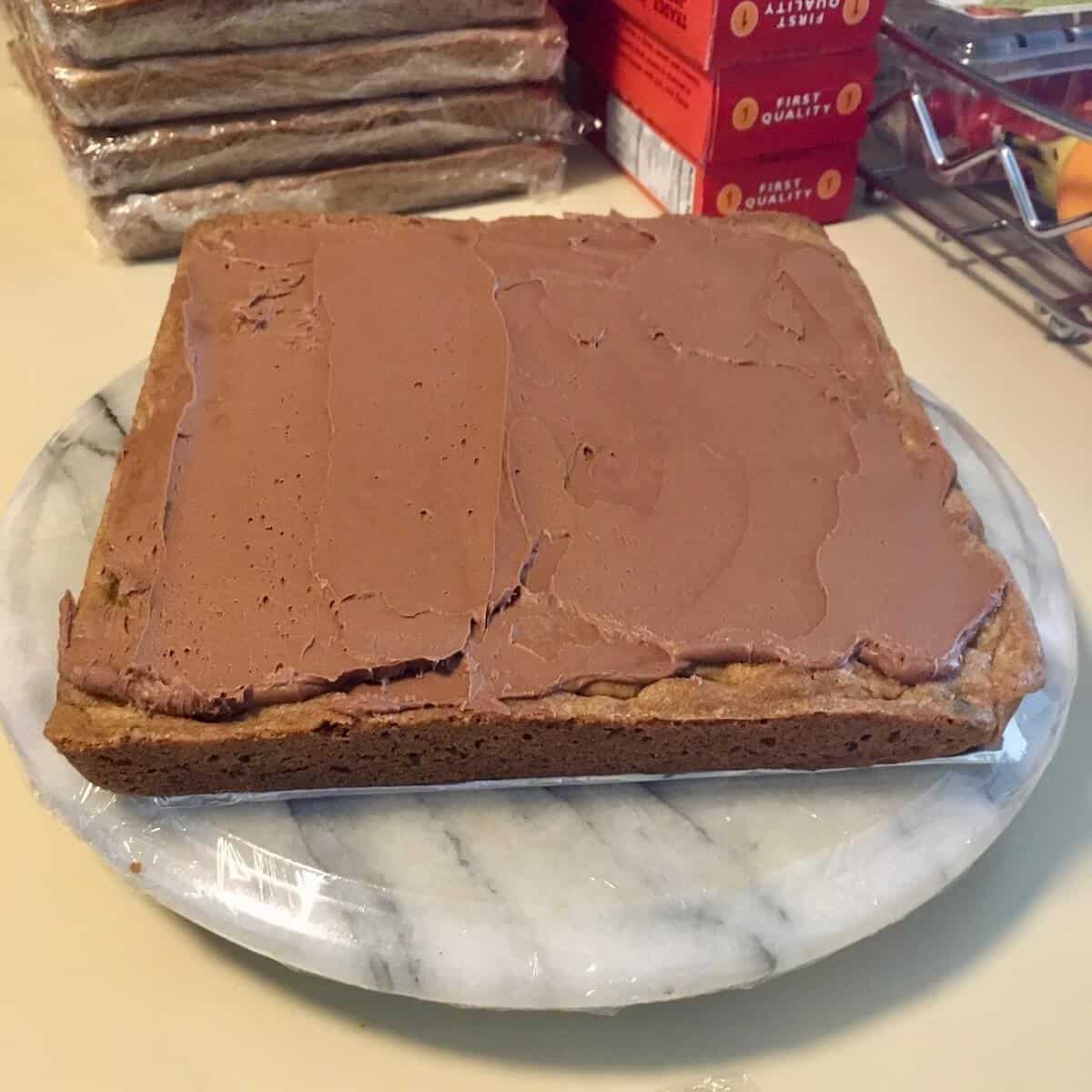 Cookie cake layer covered with chocolate buttercream frosting on a marble turntable.