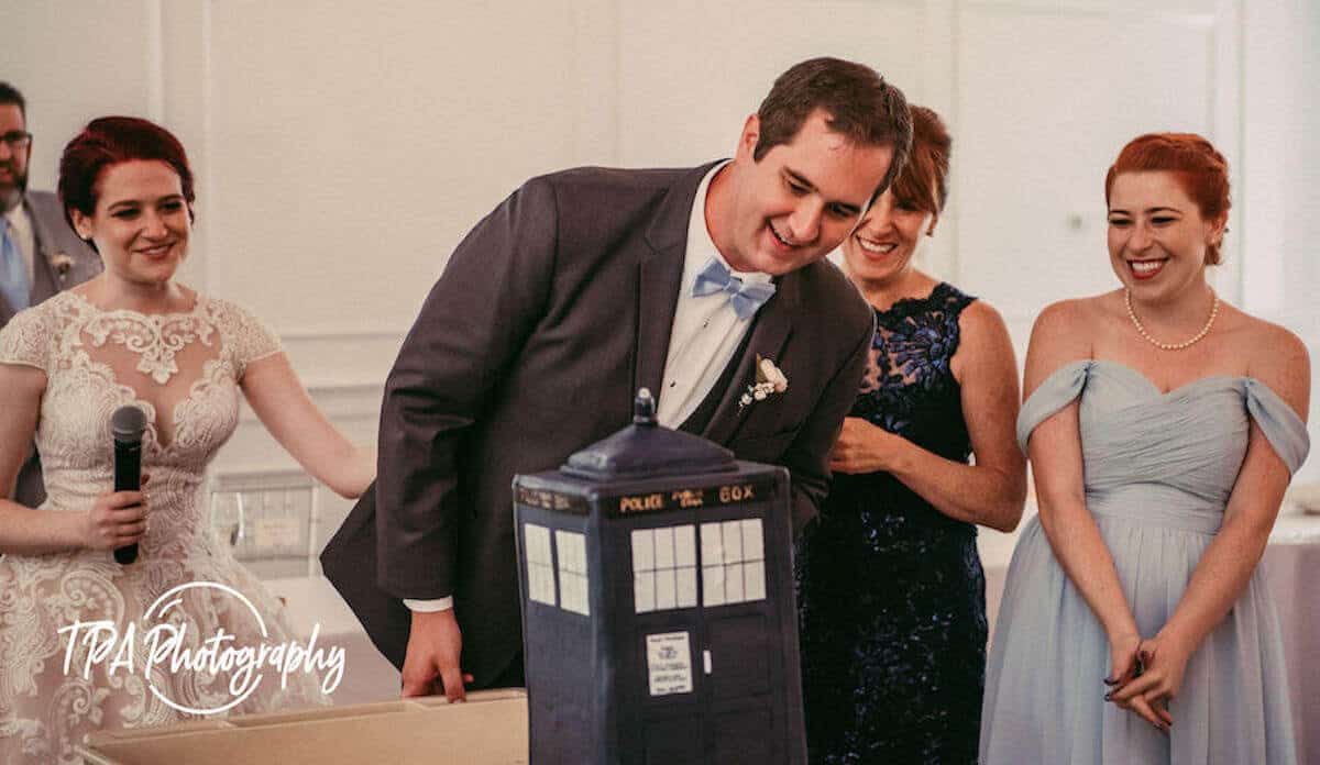 The groom looks over his TARDIS cake with the family behind him.