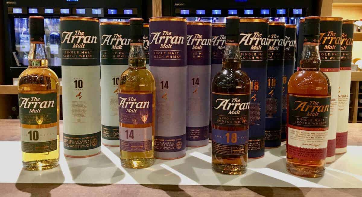 Bottles and sleeves of Arran Malt Collection scotch lineup on a counter.