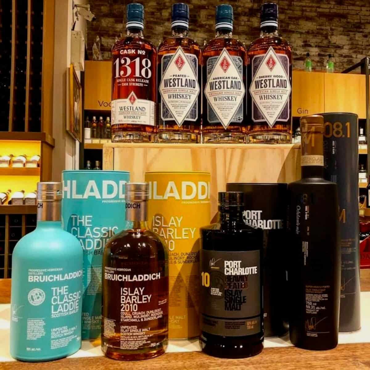 Bruichladdich, Port Charlotte, and Octomore bottles with sleeves on counter, with Westland lineup bottles behind on a crate.