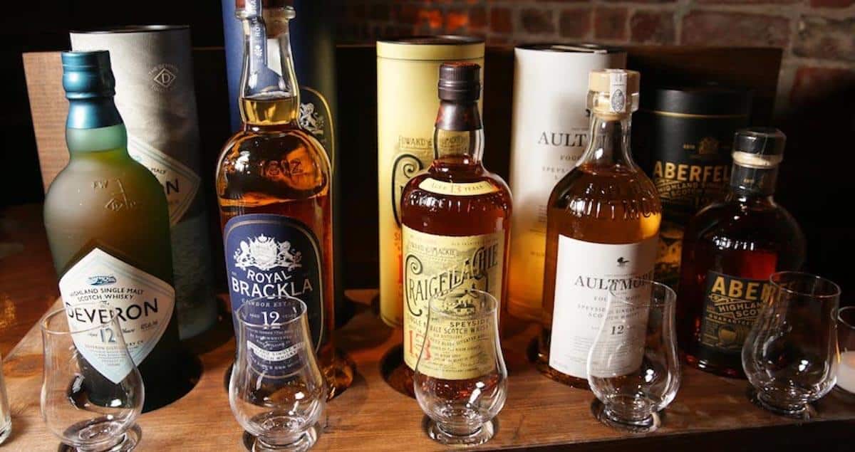 John Dewar & Sons Fine Scotch Whisky Emporium lineup in bottles behind empty glasses on a table.