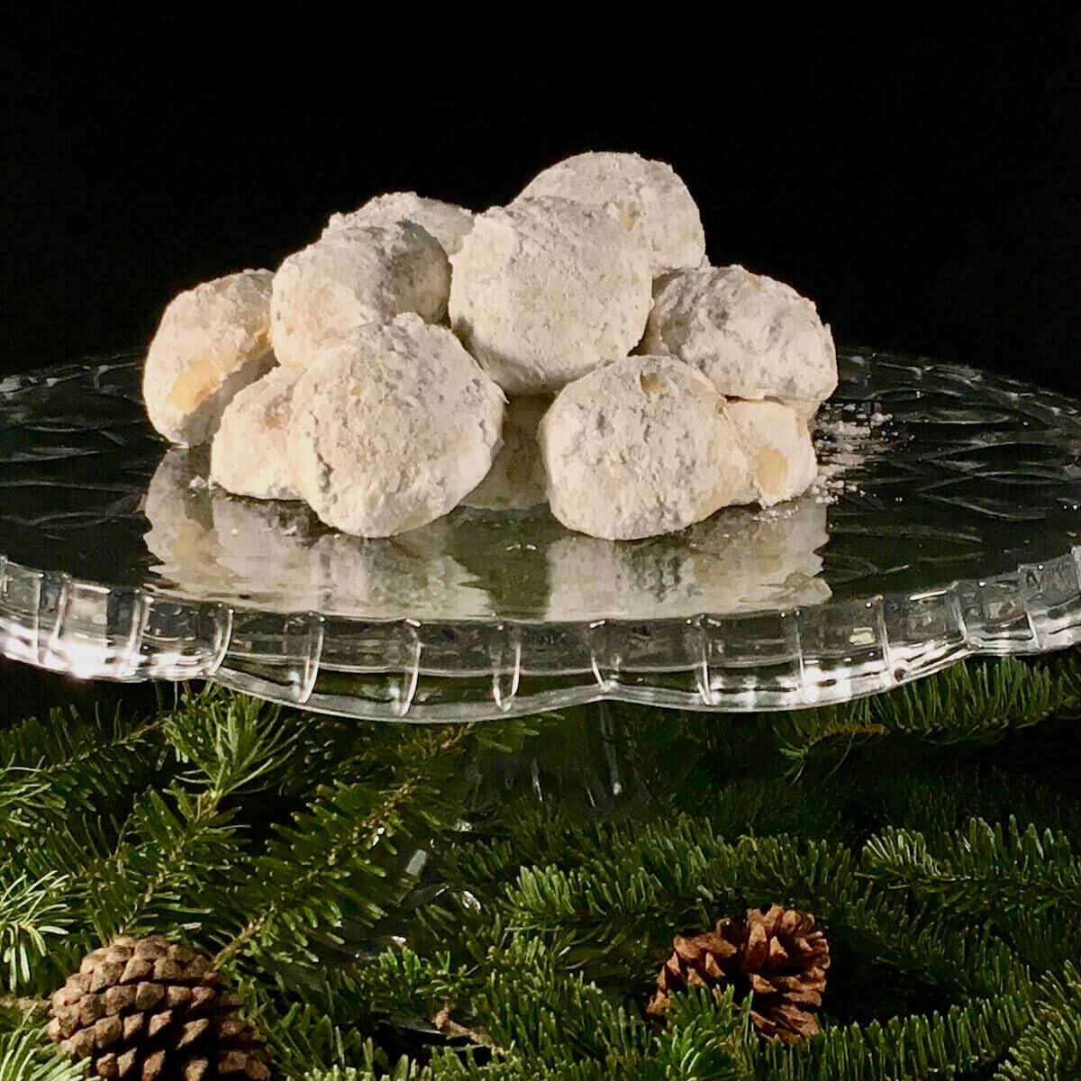 Pecan snowballs on a glass cake stand over pine cones & branches.
