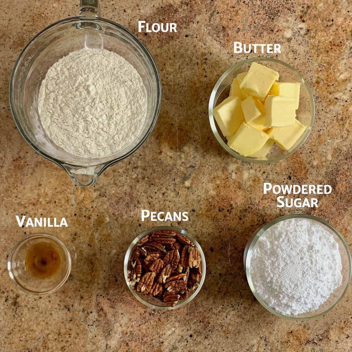 Ingredients for pecan snowball cookies portioned into glass bowls from overhead.