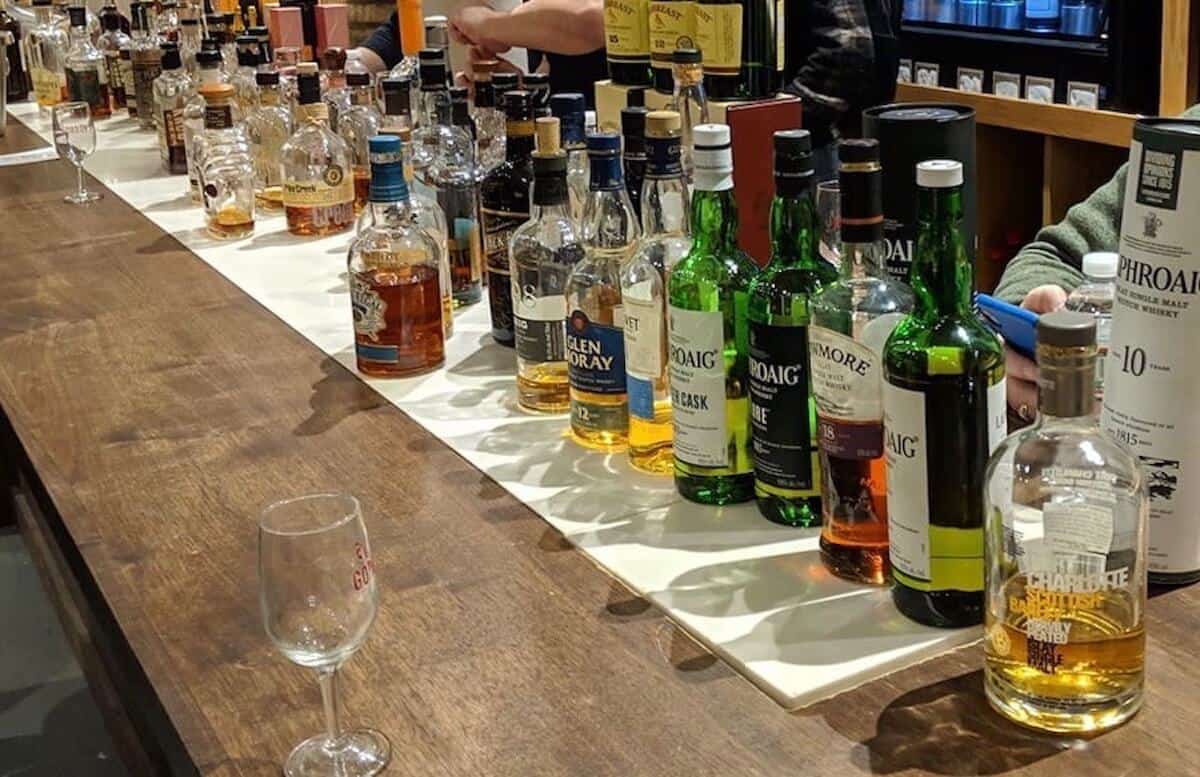 Counter full of scotch and whiskey bottles with glasses in front.