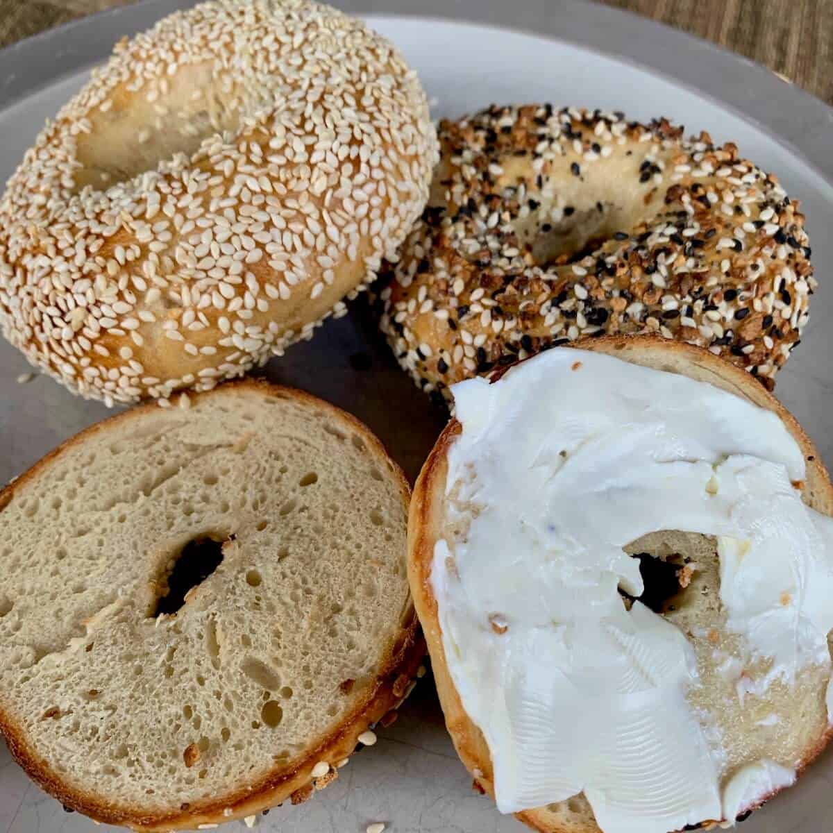 Assorted toasted sourdough bagels with cream cheese on a plate.