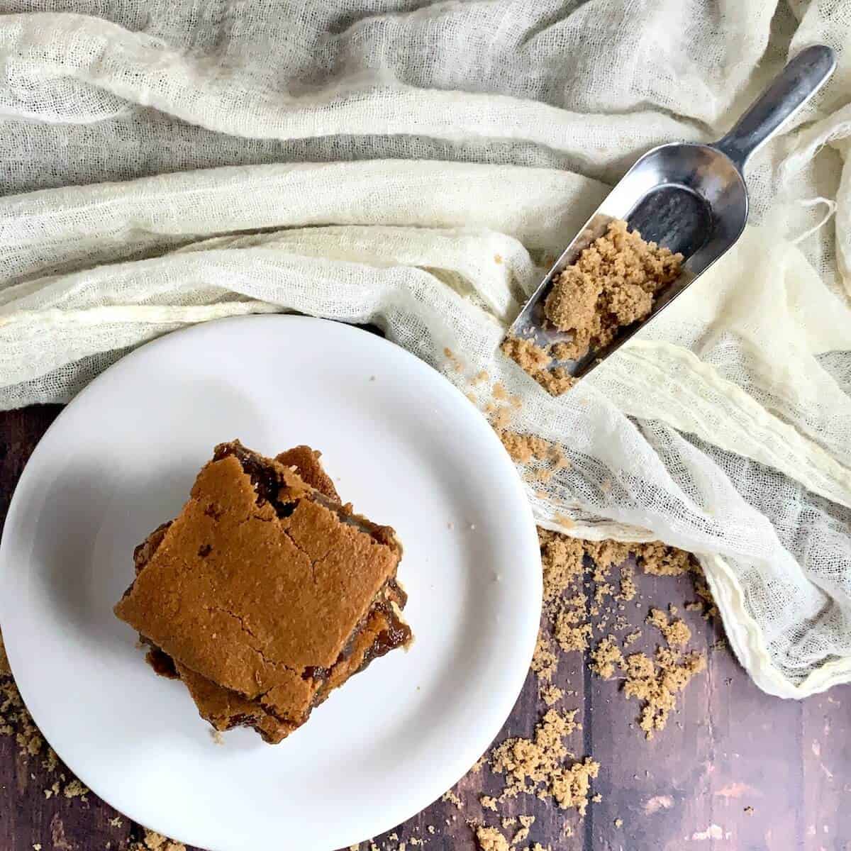 Brown Sugar Pie bars stacked on a white plate on wood table sprinkled with brown sugar viewed from overhead.