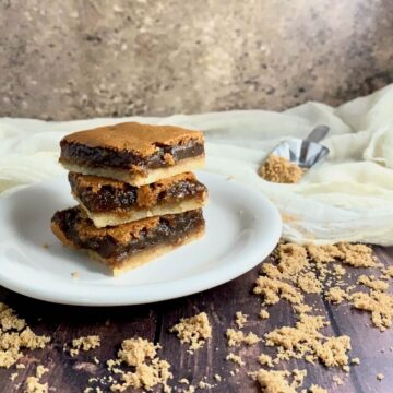 Brown Sugar Pie bars stacked on a white plate on a wood table sprinkled with brown sugar.