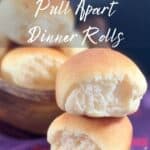 Two sourdough dinner rolls stacked on a purple checked towel with bowl of rolls in background Pinterest banner.