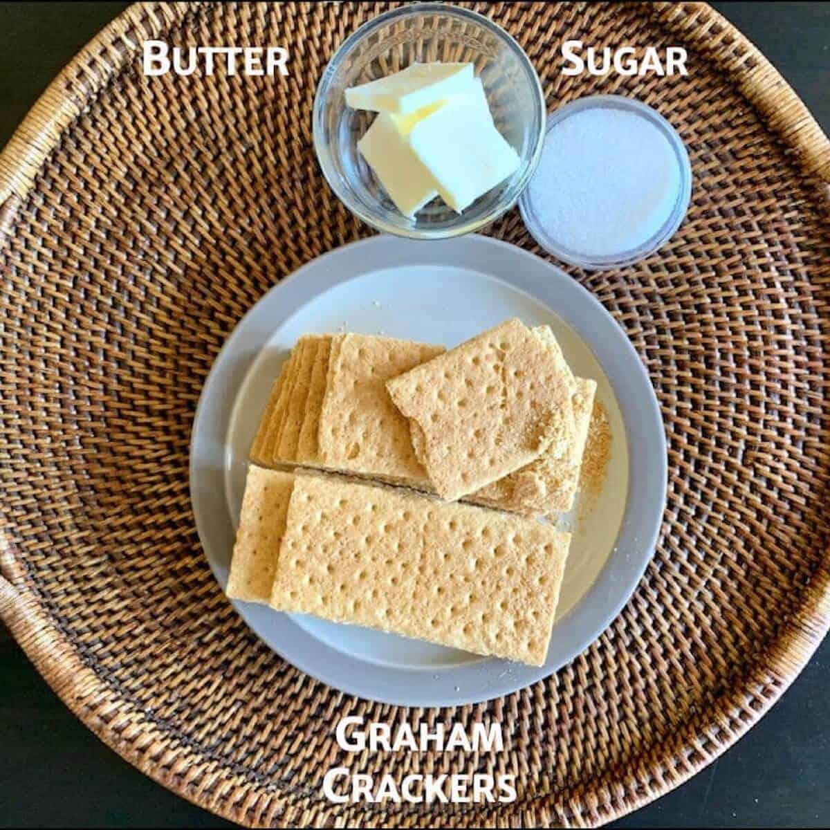 Graham cracker crust ingredients portioned in bowls on a wooden tray.