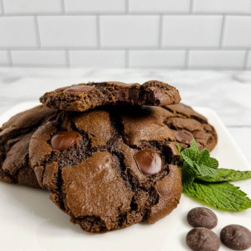 Stack of Double Chocolate Mint Cookies with the top one bitten on a white plate with mint and chocolate wafers.