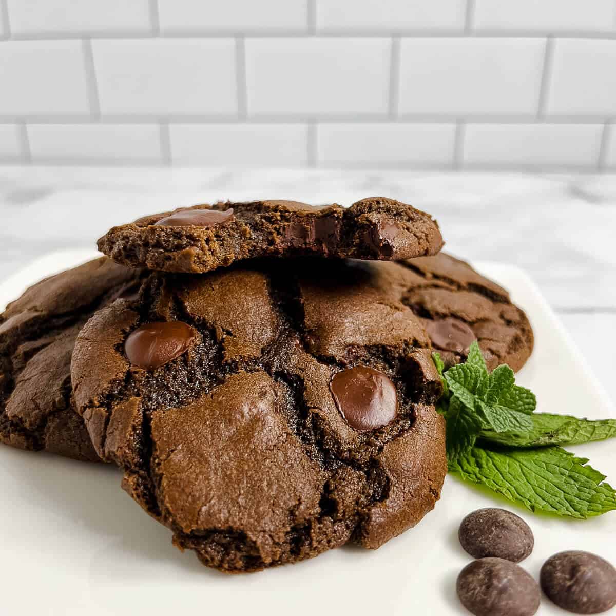 Stack of Double Chocolate Mint Cookies with the top one bitten on a white plate.