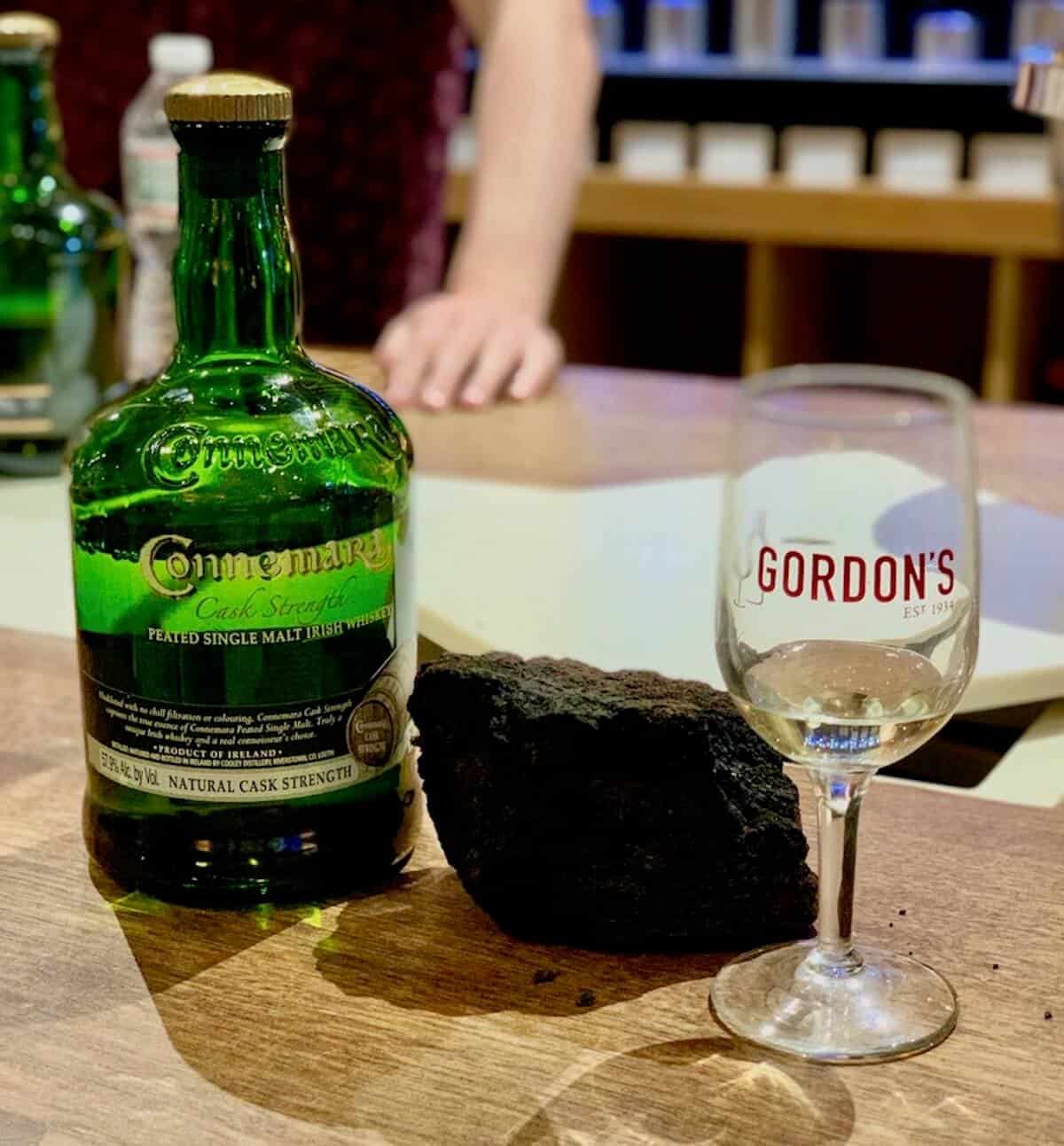 Connemara bottle with lump of peat & poured glass on a counter.