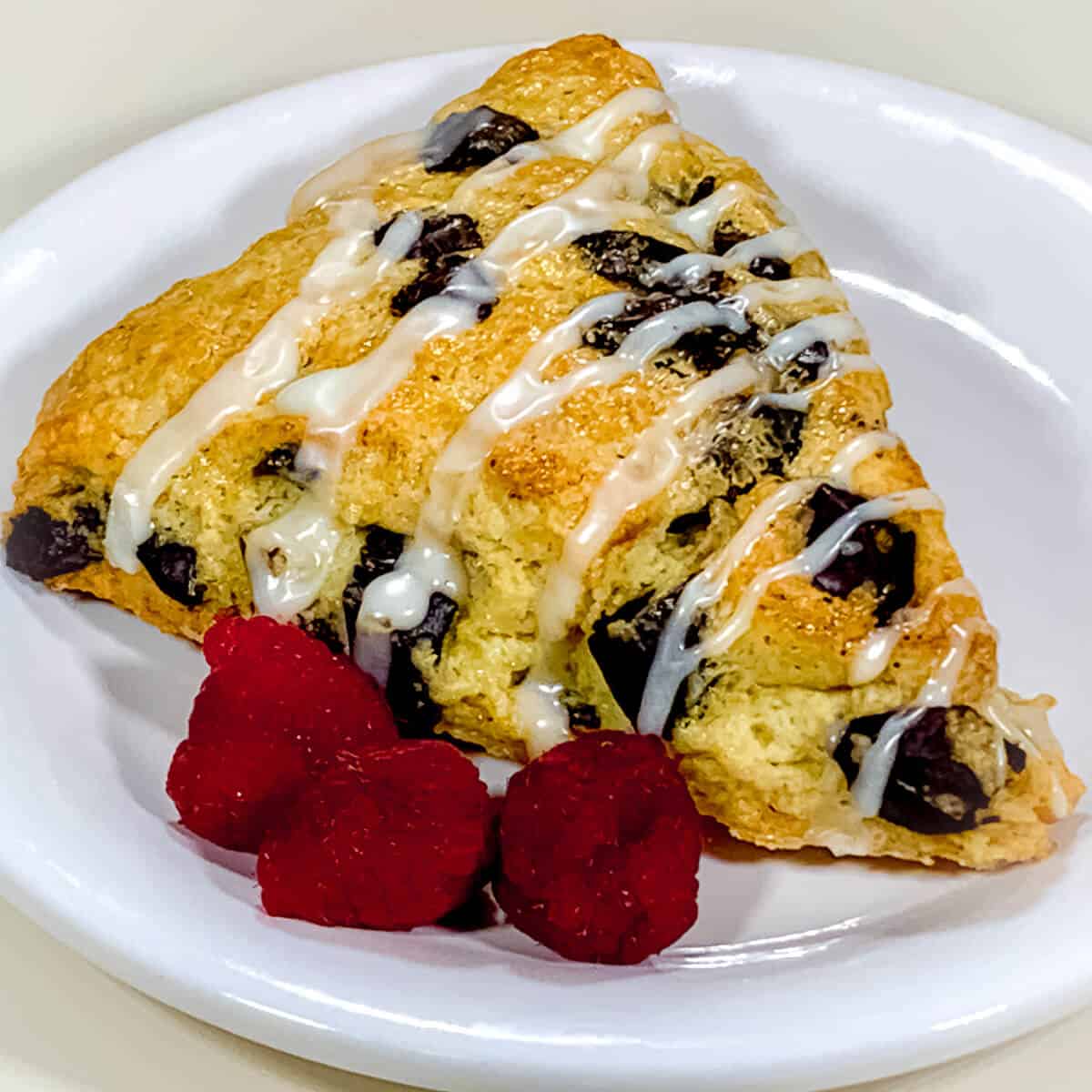 Mint chocolate chunk scone on a white plate with raspberries.
