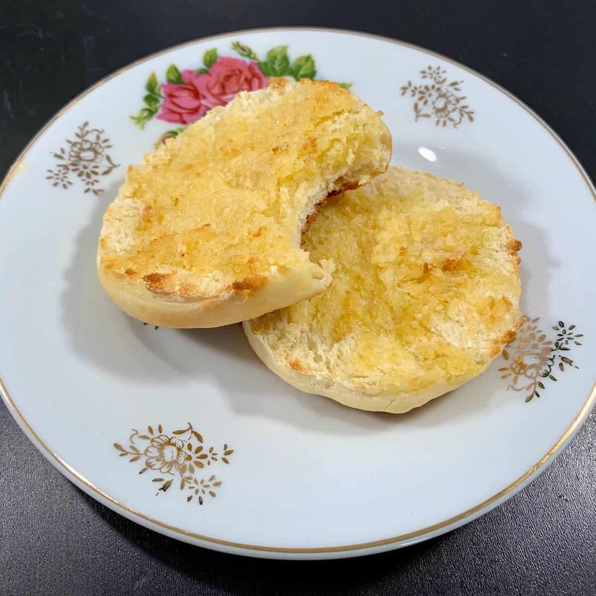 Two toasted & buttered Sourdough English Muffin halves stacked on a white plate.