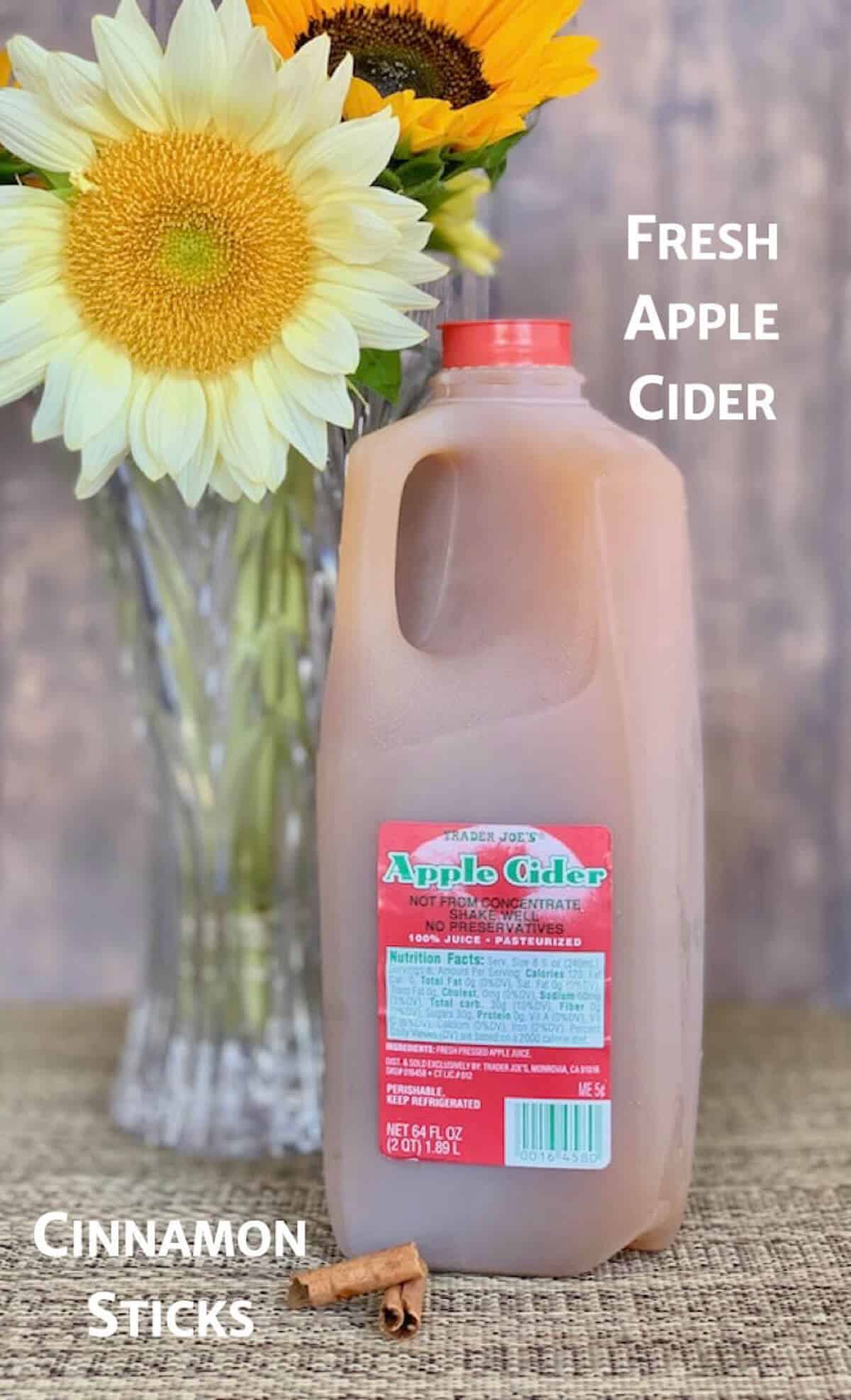 Fresh apple cider in jug with cinnamon sticks and sunflowers.