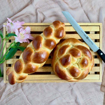 Straight challah on a cutting board with a bread knife and flowers from overhead.