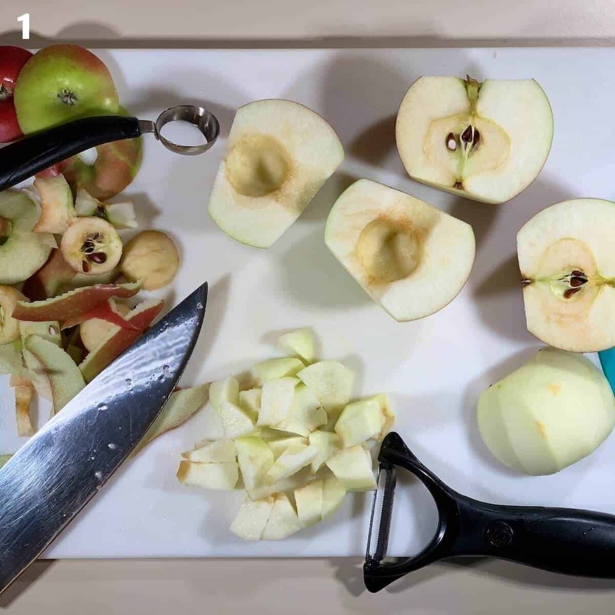Peeled & cubed apples on a cutting board with peeler, knife, and corer.
