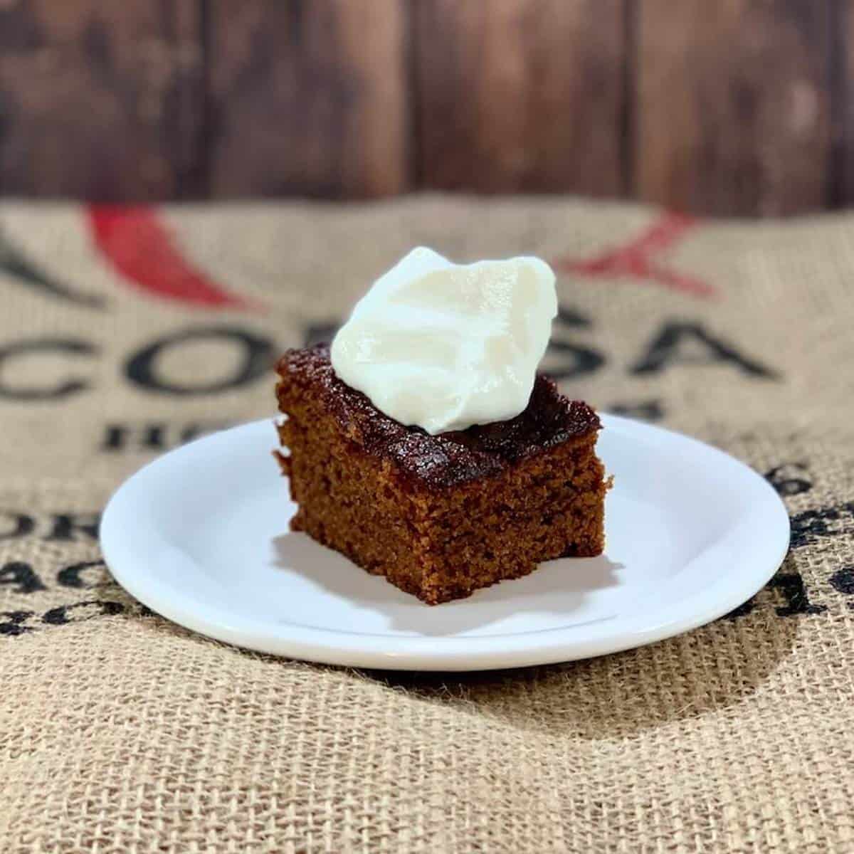 Sourdough gingerbread on a white plate topped with whipped cream.