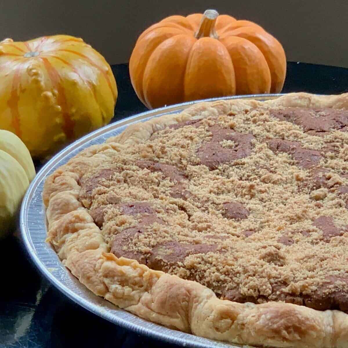 whole Shoofly pie with pumpkins on a black table.