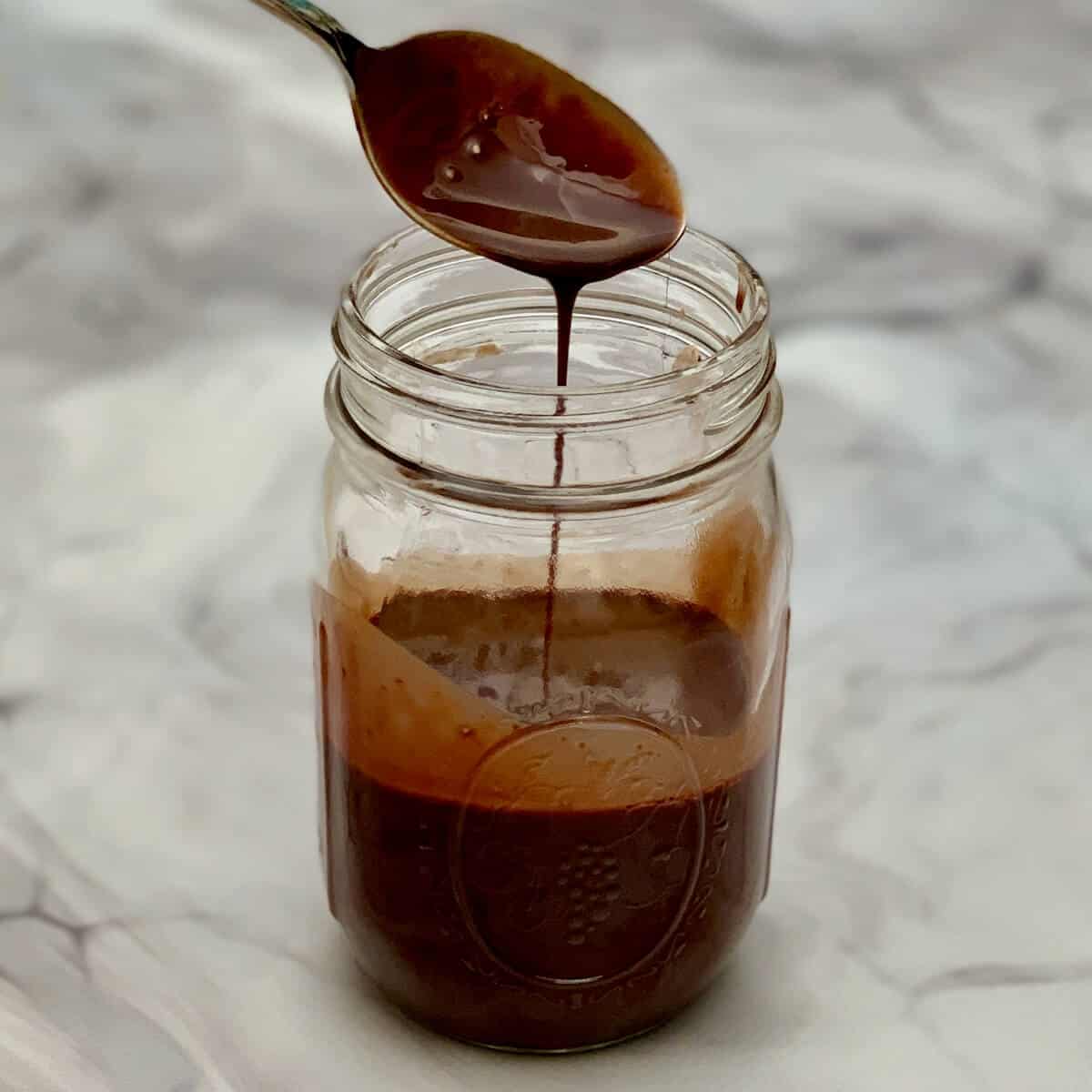 Chocolate syrup dripping from spoon into a jar.
