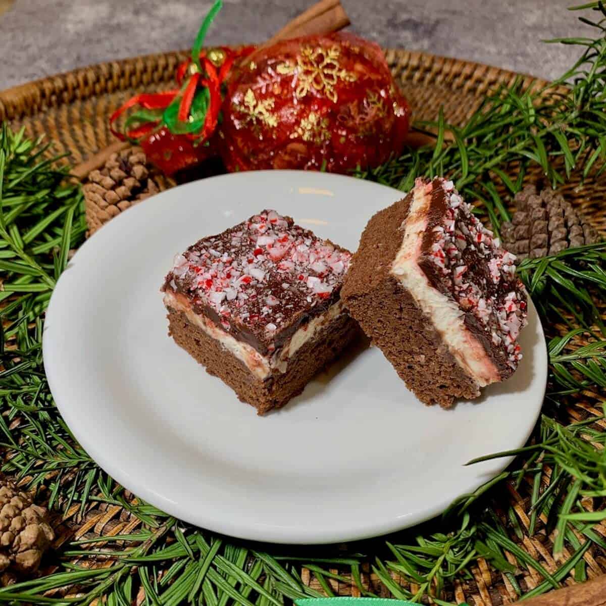 Double chocolate mint brownies on a white plate with greenery & Christmas sachet on a wooden tray.