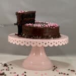 Port wine dark chocolate cake on a pink cake stand with slice lifted.