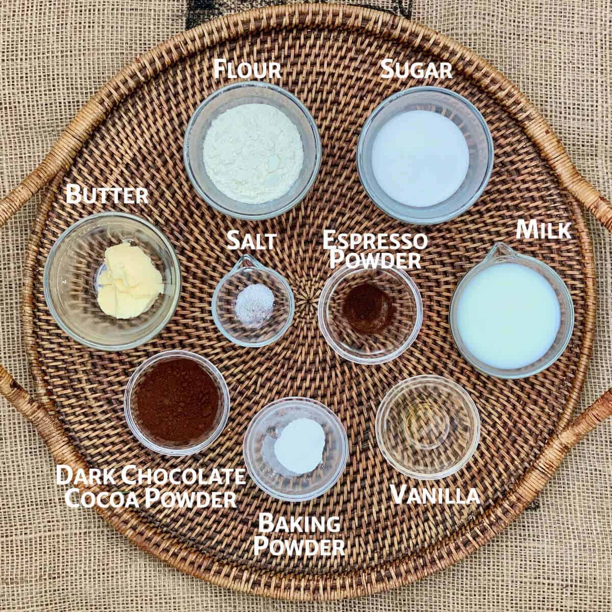 Pudding cake base ingredients portioned in glass bowls on wooden tray from overhead.