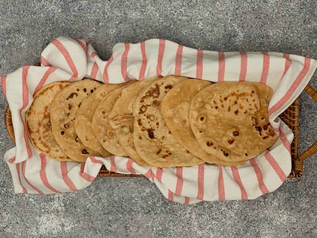 Eight sourdough naan pieces on a red & white striped towel in a basket from overhead.