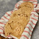 Eight sourdough naan pieces on a red & white striped towel in a basket.