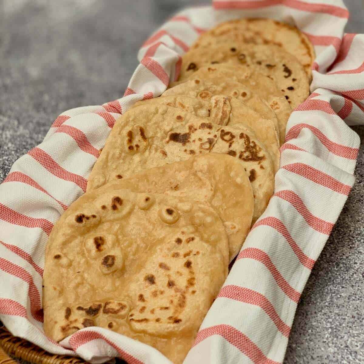 Eight sourdough naan pieces on a red & white striped towel in a basket.