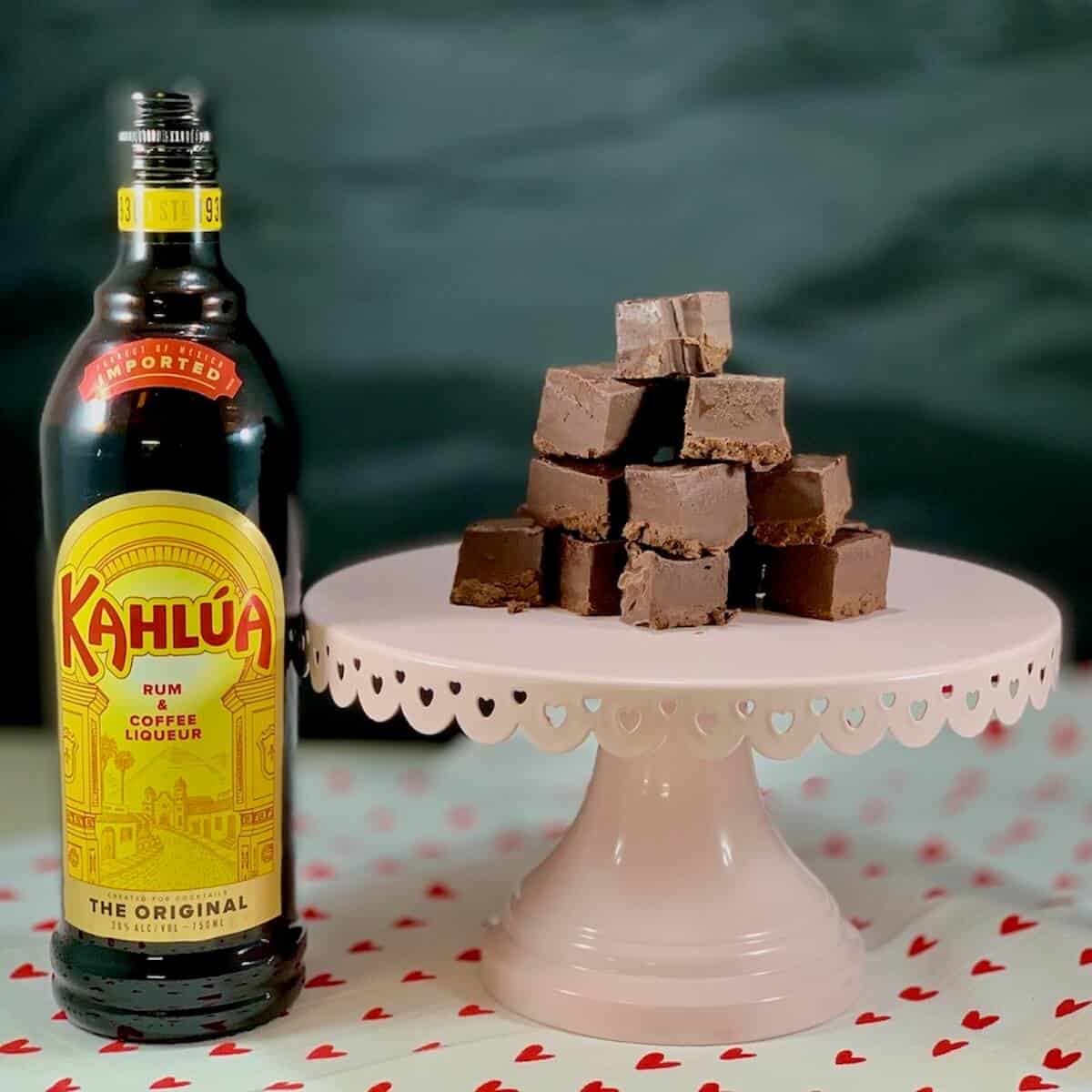 Kahlua Fudge stacked on a pink cake stand with Kahlua bottle.