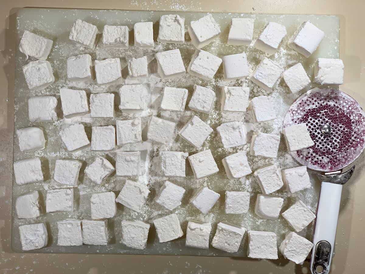 Whiskey marshmallows on cutting board with cutter.